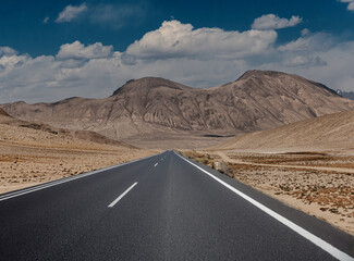 A long road stretches across a desert with mountains in the background