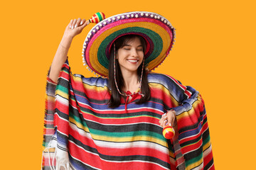 Young woman with sombrero, colorful poncho and maracas on yellow background. Cinco de Mayo celebration