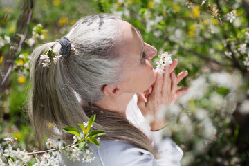  lifestyle portrait senior woman  with gray hair relaxes in a flowering garden in spring. spends...