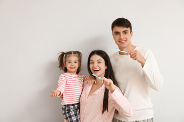 Happy family with cute little daughter brushing teeth on white background