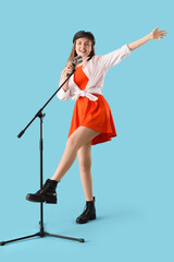 Fototapeta premium Young woman with microphone singing karaoke on blue background