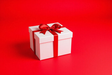 Fototapeta premium Beautifully styled white gift box with red ribbon on vibrant red background