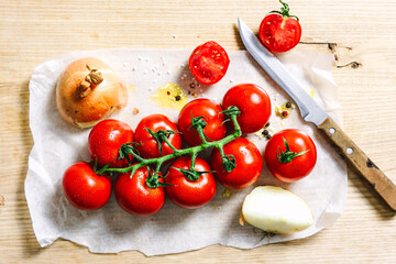 Frische Cocktailtomaten an der Rispe mit Zwiebeln und Olivenöl auf einem Backblech. Grillen,...