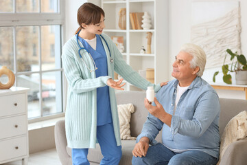 Obraz premium Female doctor and mature man with pills sitting on sofa at home