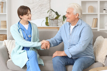 Obraz premium Female doctor with mature man holding hands on sofa at home