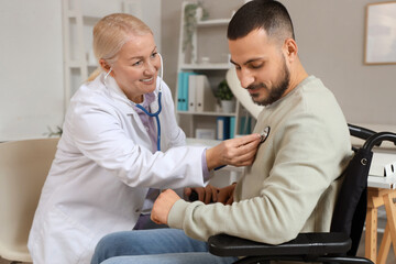 Obraz premium Female doctor with stethoscope listening to young man in wheelchair at hospital