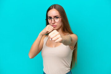 Young caucasian woman isolated on blue background with fighting gesture