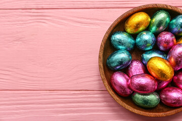 Bowl of chocolate Easter eggs in foil on pink wooden background