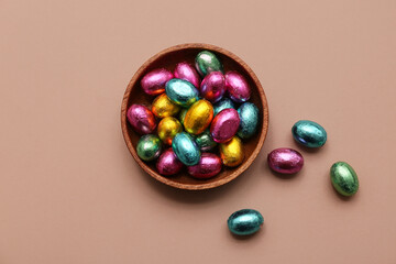 Bowl of chocolate Easter eggs in foil on beige background