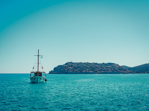 Ein kleines Segelboot auf der R&uuml;ckkehr von der Insel Spinalonga, Kreta, Griechenland mit der griechischen Flagge