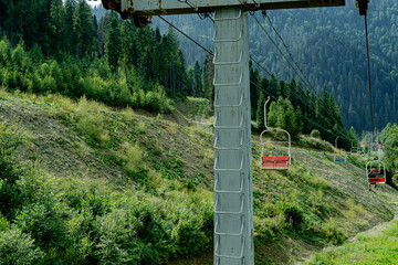 Ski lift in green forest. Cableway in Mountains. Summer nature outdoor trees