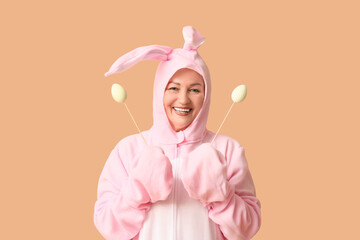 Funny senior woman in bunny costume with Easter eggs on beige background