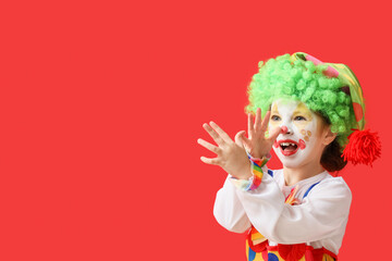Little girl in clown costume grimacing on red background. April Fools' Day celebration