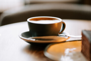 Richly brewed coffee served in a stylish cup on a wooden table next to a chocolate dessert in a cozy cafe setting