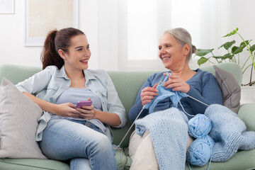 Happy family at home, smiling daughter using her smartphone, while smiling senior mother is sitting...