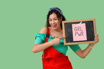 Young African-American pin-up woman pointing at GRL PWR sign on chalkboard against green...