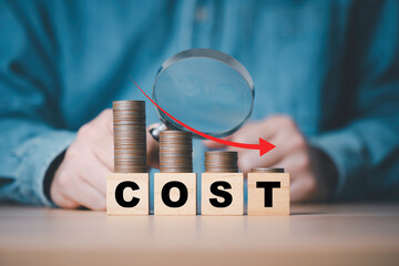 Businessman  use magnifier glass and down arrow with decreasing of coins stacking for cost...