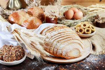 A large loaf of bread sliced for sandwiches. Surrounded by rolls and cookies.