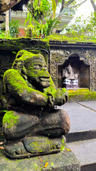 A moss-covered Balinese statue sits peacefully near an intricately carved shrine, surrounded by lush greenery and traditional stonework, reflecting spiritual harmony and ancient craftsmanship.