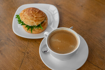 Top view of a breakfast scene featuring a flaky croissant sandwich filled with fresh greens and paired with a steaming cup of rich café crema. Cozy and elegant breakfast concept.