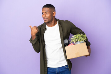 Latin man making a move while picking up a box full of things pointing to the side to present a...
