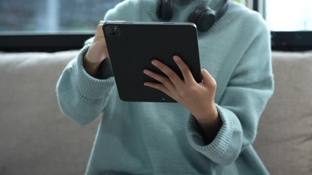 Smiling woman in headphones taking notes, motivated interested student studying online, using tablet, watching webinar training or listening to lecture, remote education concept.