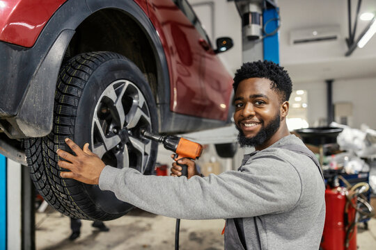 Portrait of smiling multicultural car mechanic changing tires at auto mechanic workshop.