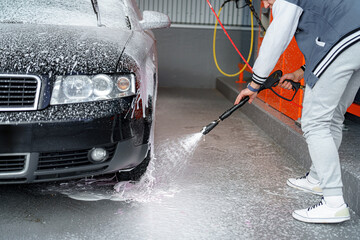 A man applies foam to a car to remove dirt at a car wash.