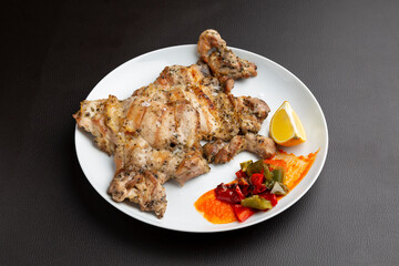 Grilled chicken thighs garnished with fresh herbs, accompanied by roasted peppers and zesty lemon wedge