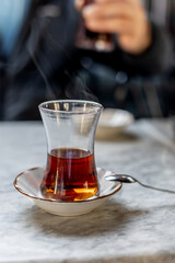 Turkish tea in a traditional glass half-full with small spoon on a gray marble table background close-up vertical