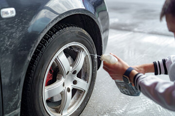 A driver applies cleaning agent to wheels at a car wash.