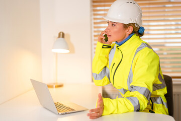 Female Construction site manager in high-visibility safety gear communicates with team using laptop in productive work environment 