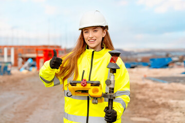Portrait of a young female Construction site surveyor wearing safety gear smiles and gives a...