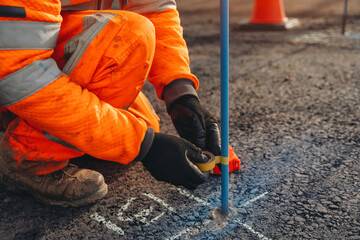 Builder fitting a colour tape on road pin as a level reference point for kerb line and asphalt level 