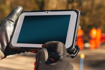 Close-up of Digital touchscreen controller device held by a builder on a construction site during daytime with blurred figures in the background