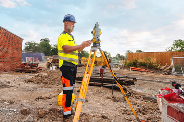Land Surveyor Site engineer conducting measurement at a construction site in daylight using a total station for land surveying