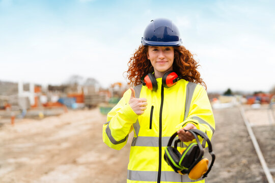 Female builder demonstrating safety measures at a building site during daylight, highlighting the importance of hearing protection