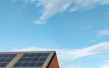Fototapeta premium Solar panels installed on a modern building roof under a clear blue sky with scattered clouds during the day
