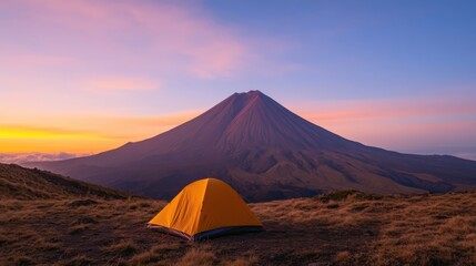 Fototapeta premium Scenic sunrise hike leading to the summit of a majestic snow capped mountain with a lone camping tent in the foreground against the backdrop of a colorful sky and rugged landscape
