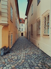 A charming cobblestone alley in Prague, lined with pastel-colored historic buildings with red-tiled roofs. Peaceful street exudes old-world European charm, perfect for exploring Prague’s hidden gems.