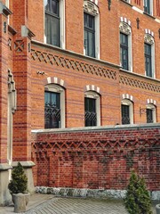 Stunning red brick neo-Gothic building in Kraków, Poland, showcasing intricate architectural details, arched windows, and decorative elements. The historic facade stands out against a bright blue sky.