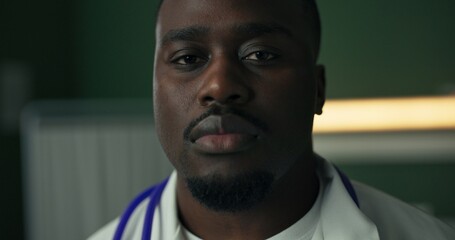 Young African doctor, dressed in a white coat with a stethoscope, gives a serious look.