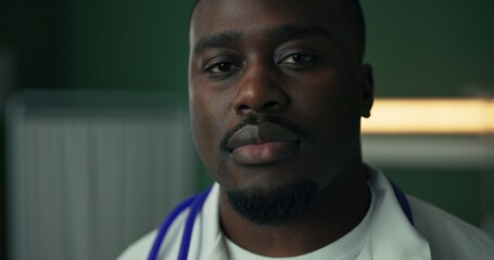 In a hospital setting, a young African physician poses with a warm smile, stethoscope draped around his neck, and dressed in a white coat.