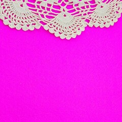White lace doily on a bright pink background, top left corner