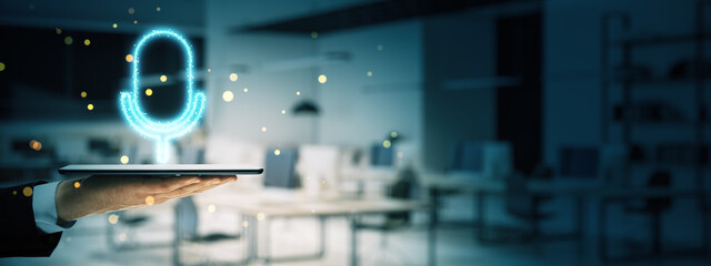 Glowing microphone hologram hovering over a tablet screen in a modern office setting.