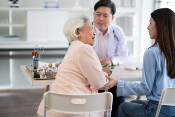 Fototapeta premium Elderly Asian senior woman in old rose shirt see doctor with her daughter, Old woman got pain meet doctor to cure her disease.