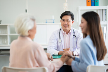 Asian male doctor  give health advise to young woman and old woman at hospital kindness and warm. Out of focus young beautiful woman holds her mother hand give encoragment.