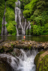 Obraz premium A Banyumala Twin Waterfalls gracefully cascades into a pristine, crystalclear pool, where girl relax, embraced by vibrant, lush foliage perfect escape into the serene beauty of nature, Bali, Indonesia