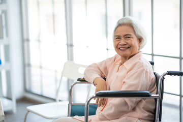 Eldery Asian senior woman in old rose shirt sitting on wheelchair looking at camera, teeth smile,...