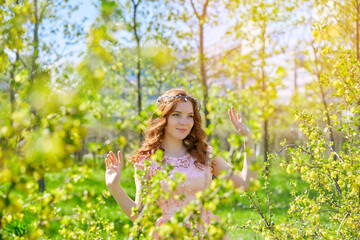 A woman with long red hair stands in a blooming garden in spring. She is wearing a pink dress, her hair fluttering in the wind. The scene is peaceful and serene.